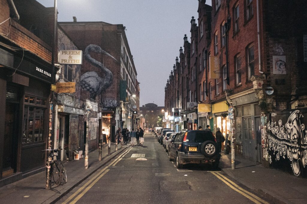 Busy Brick Lane street with a parked SUV and some people crossing the road